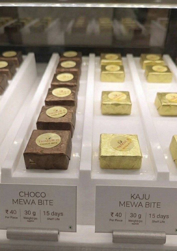 Choco Mewa Bite and Kaju Mewa Bite, individually wrapped, on display at Thakur Ji Sweets